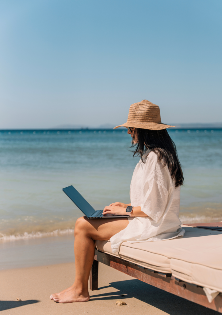 Photo d'une Femme entrepreneure digitale travaillant sur son ordinateur depuis une plage, illustrant la liberté financière et le travail en ligne